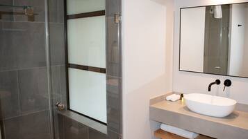 Un baño moderno con cabina de ducha de vidrio, un lavabo blanco y un espejo encima.