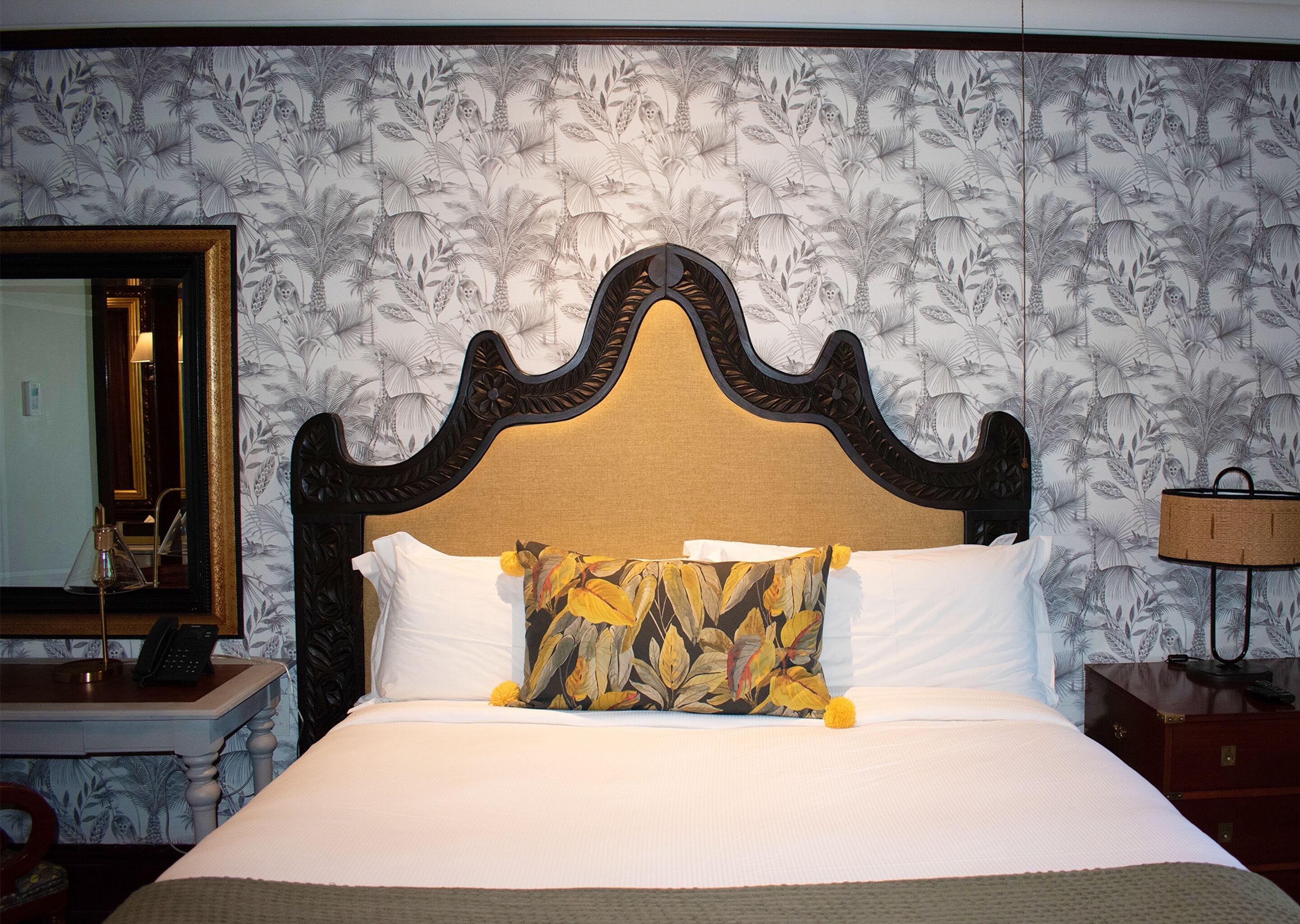 A neatly made bed with a decorative headboard, a bedside table with a lamp, and a mirror on the wall.