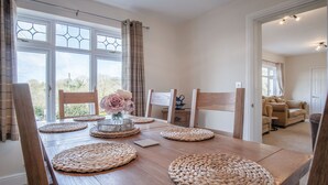 A dining area with a wooden table, woven placemats, and chairs. - Sorrento - 3 Bed Holiday Home - Wisemans Bridge (Narberth)