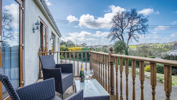 A balcony with wicker furniture, a glass table, and a bottle of champagne. - Sorrento - 3 Bed Holiday Home - Wisemans Bridge (Narberth)