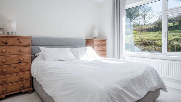 Une chambre à coucher avec un lit, une commode en bois et une fenêtre donnant sur un paysage verdoyant.