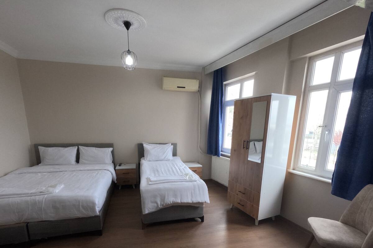 Une chambre d’hôtel avec deux lits, une armoire, une chaise et une fenêtre avec des rideaux.