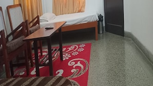 A small, simple room with a bed, a table, and two chairs. - Mehaa Paradise Family Guest House (Puducherry)