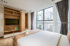 Habitación de hotel con cama, televisor montado en la pared, una mesita con una planta y una ventana con cortinas.