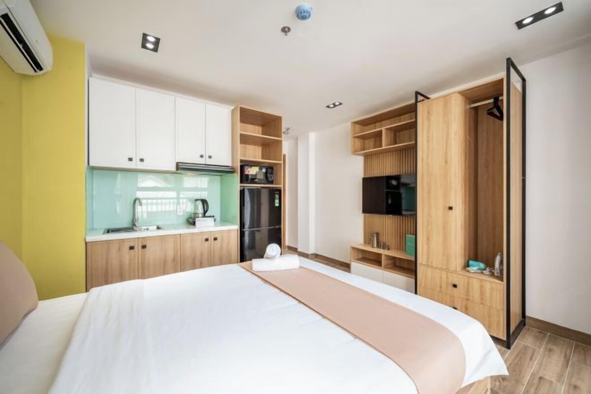 Quarto de hotel moderno com cama, cozinha compacta e armário embutido.