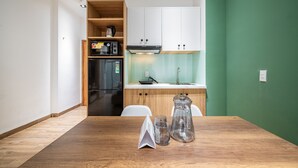 Una cocina compacta con armarios blancos, un refrigerador de acero inoxidable y una mesa de madera con una jarrón y vasos.