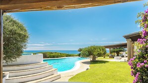 Una piscina con escalones que bajan al agua, rodeada por un césped cuidado y vistas al mar.