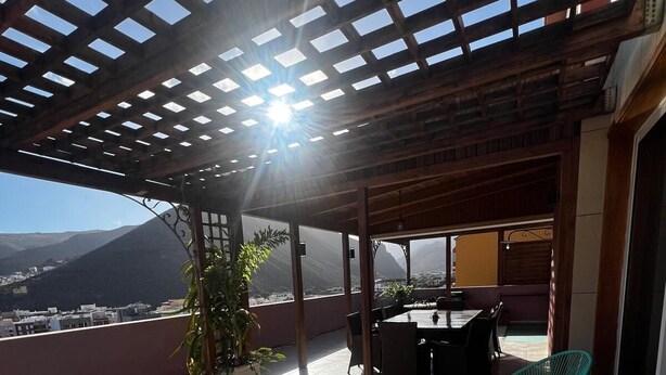 A covered outdoor patio with a view of mountains, a barbecue area, and lounge chairs. - Gomera Isla Mágica (San Sebastián de La Gomera)