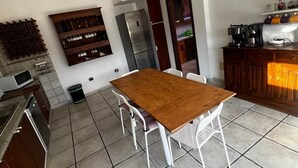 A modern kitchen with a wooden dining table, white chairs, a built-in wine rack, and a refrigerator. - Gomera Isla Mágica (San Sebastián de La Gomera)