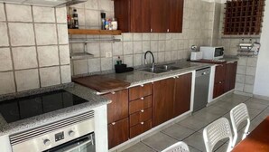 A compact kitchen with a built-in stove, a microwave, and a sink. There are wooden cabinets and a countertop. Two white chairs are visible. - Gomera Isla Mágica (San Sebastián de La Gomera)