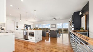 A modern kitchen with a central island, wooden flooring, and large windows offering a view of the outdoors.