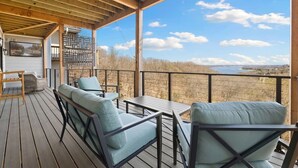 A wooden deck with outdoor seating, a view of the landscape, and a building in the background.