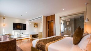 A modern hotel room with a large bed, a seating area, a TV, and a glass shower enclosure. - Yashshree Imperial  (Siliguri)