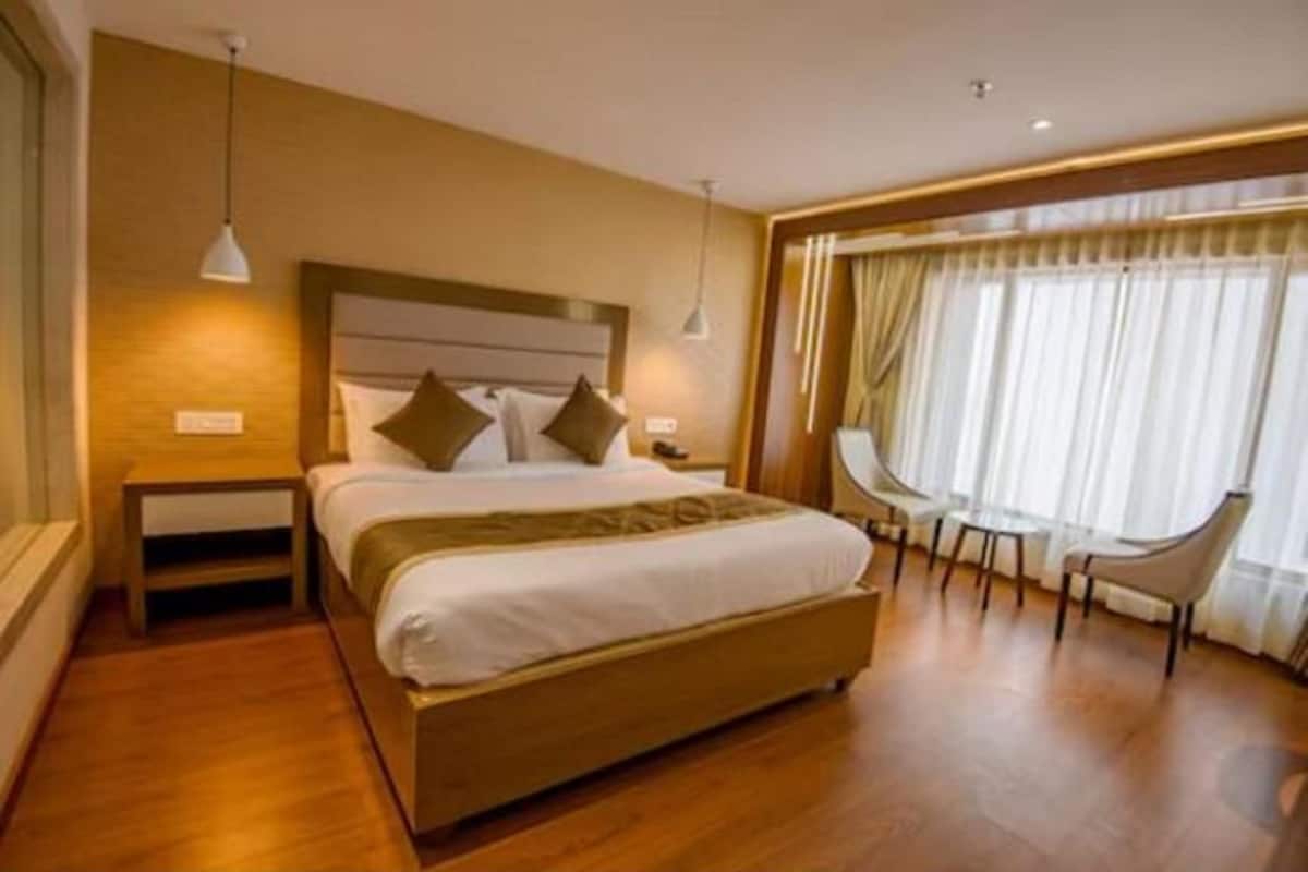 A hotel room with a large bed, bedside tables, a desk, and a window with curtains.