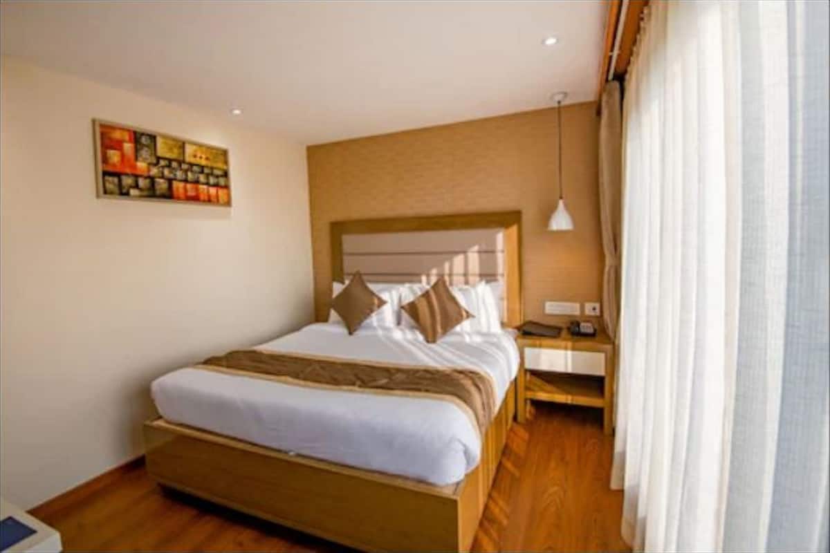 A hotel room with a large bed, a nightstand, a lamp, and a painting on the wall.