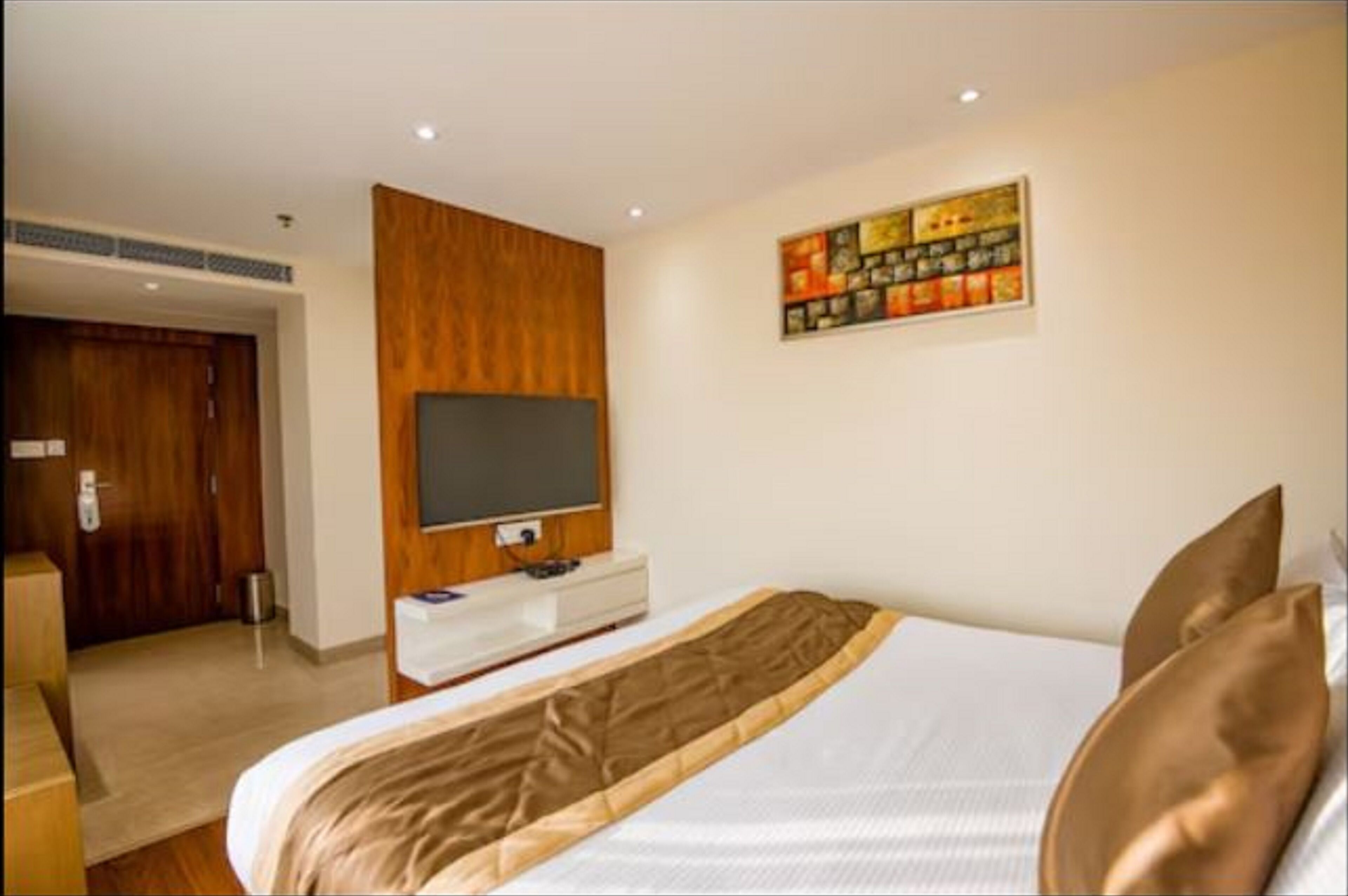Habitación de hotel con cama, televisión montada en la pared, panel de pared de madera y un cuadro sobre la cama.
