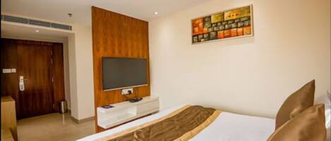A hotel room with a bed, a television mounted on the wall, a wooden panel wall, and a painting above the bed.