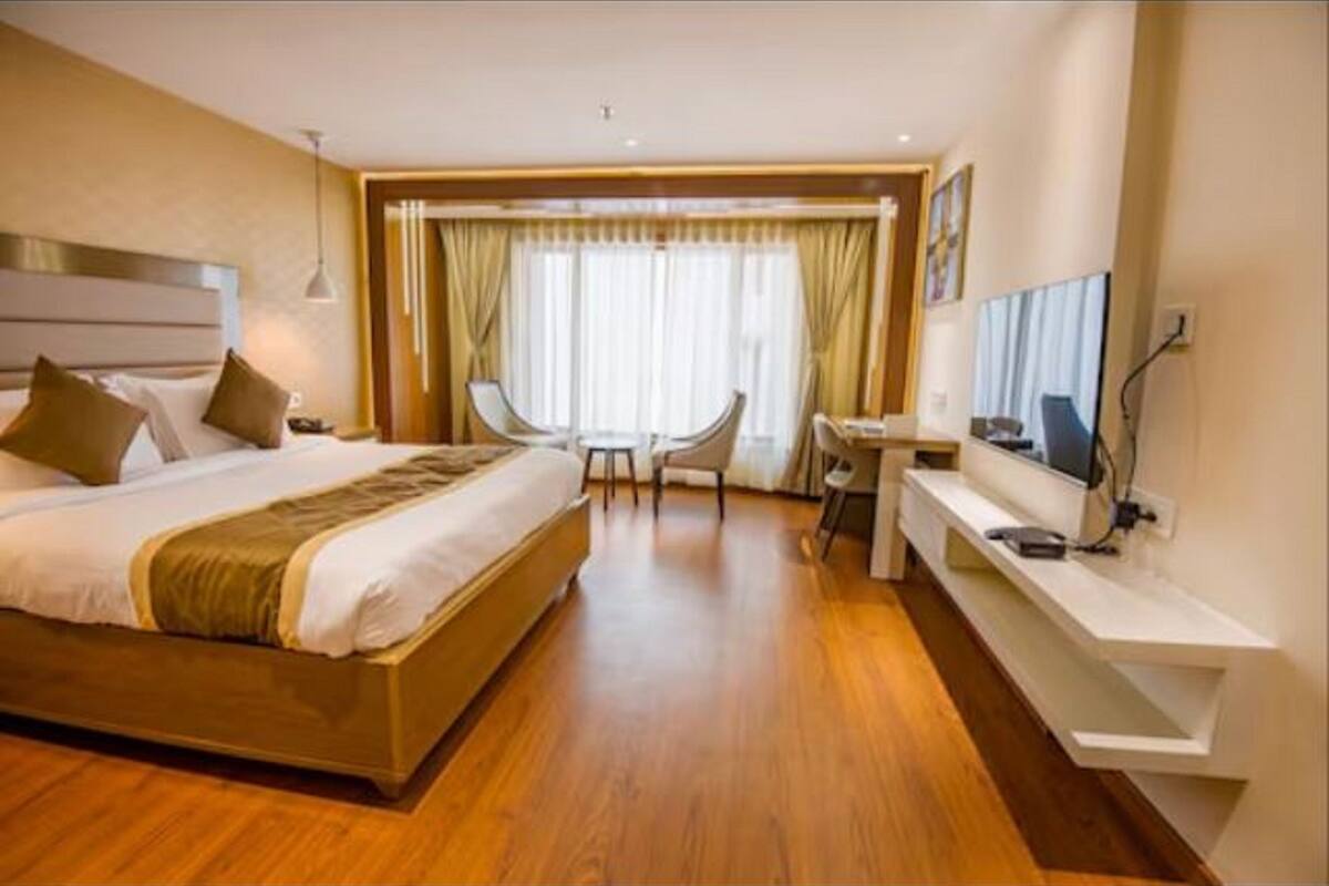 A hotel room with a large bed, a desk with a chair, a television, and a window with curtains.