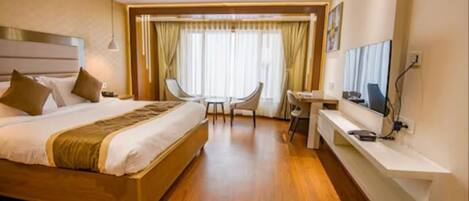 A hotel room with a large bed, a desk with a chair, a television, and a window with curtains.