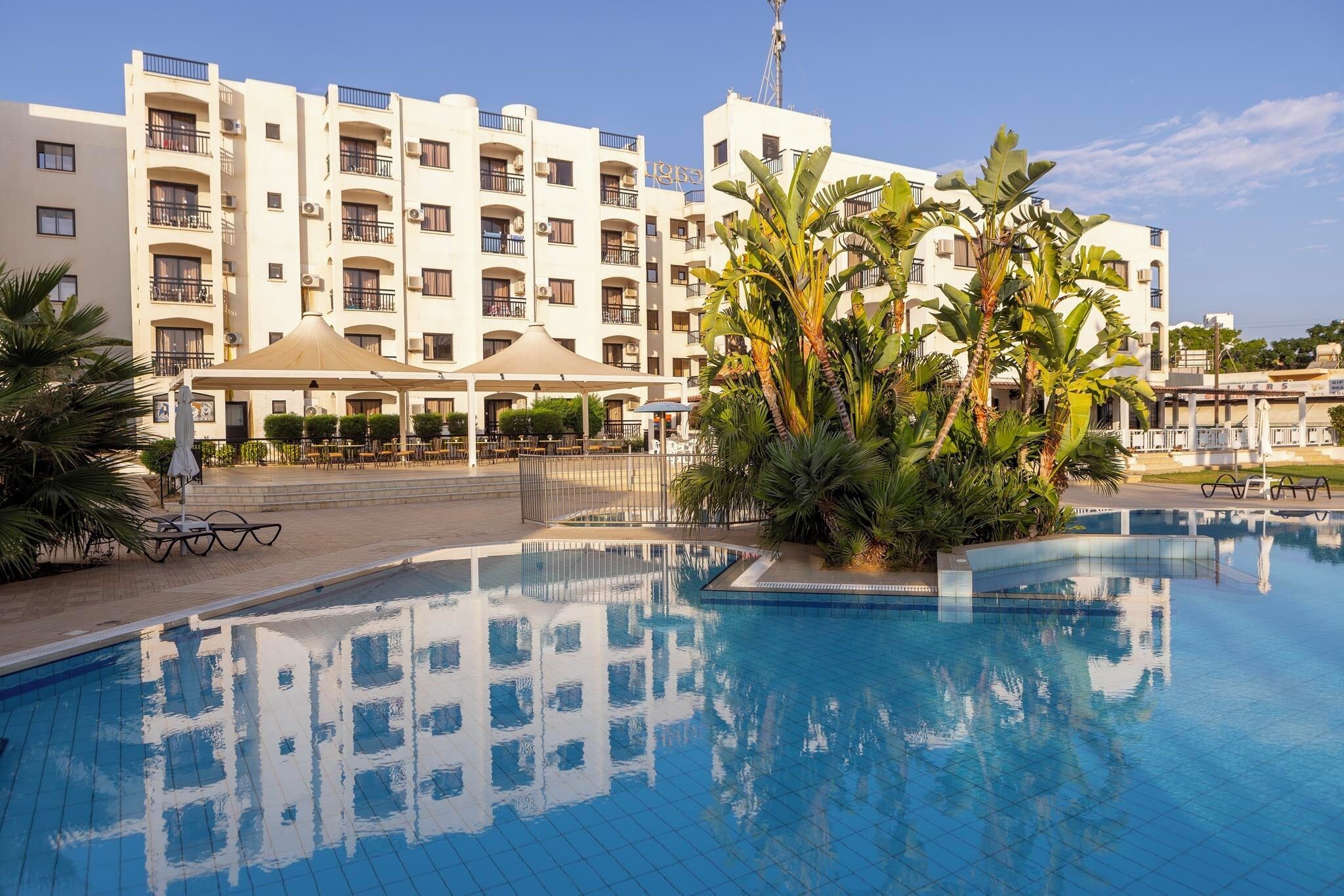 A hotel with a swimming pool, outdoor seating, and a large building with balconies.