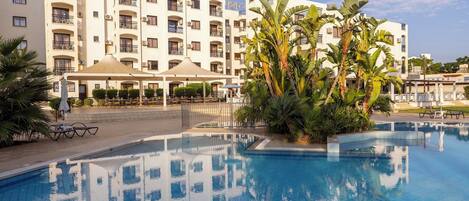 A hotel with a swimming pool, outdoor seating, and a large building with balconies.