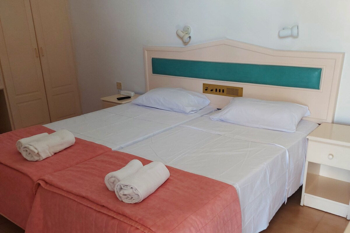 A hotel room with a bed, a nightstand, a telephone, and a wardrobe.