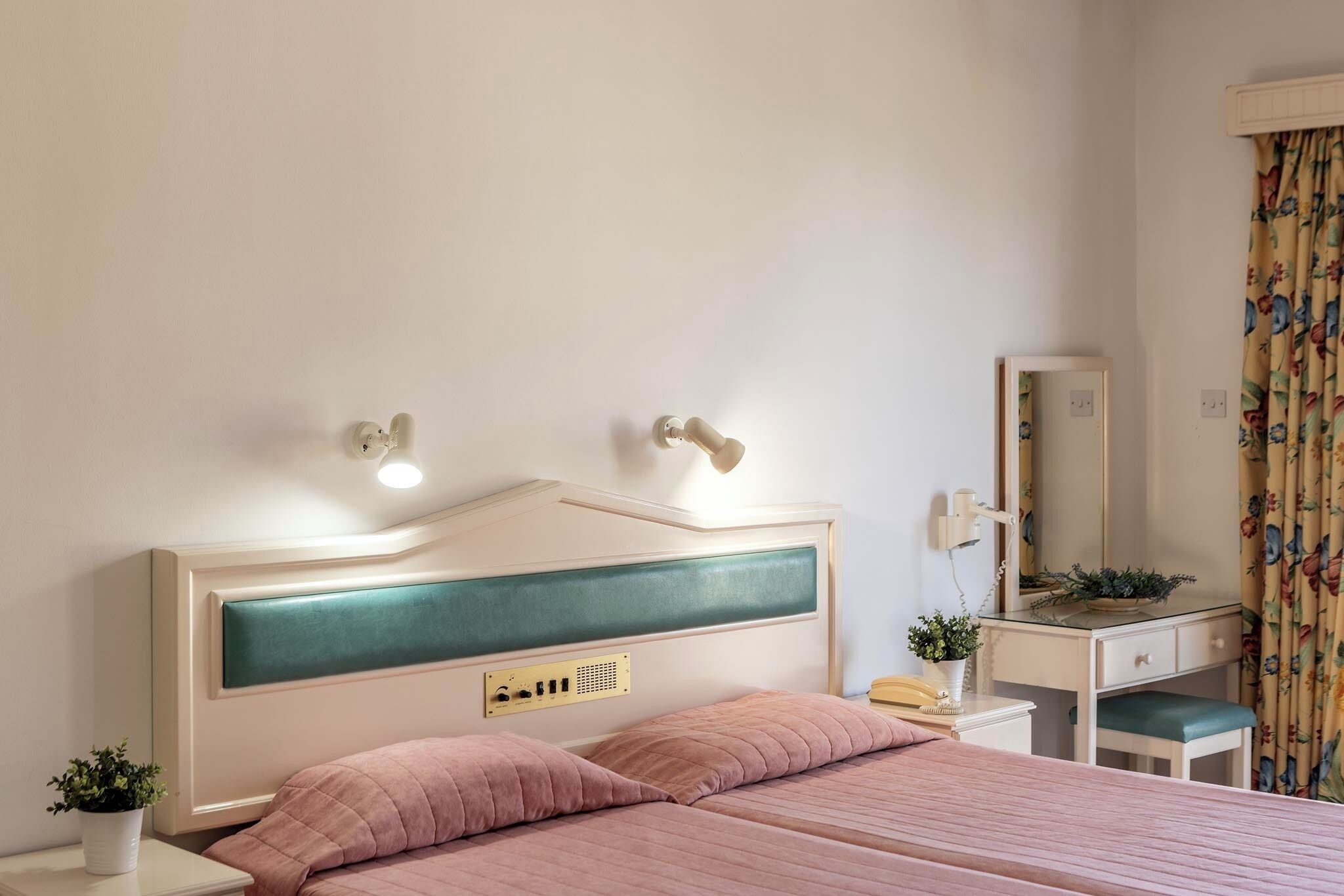 Una camera da letto con un letto, un comodino, una lampada, uno specchio e una piccola pianta.
