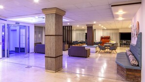 Un vestíbulo amplio con una zona de estar central, un mostrador de recepción y un letrero de salida.