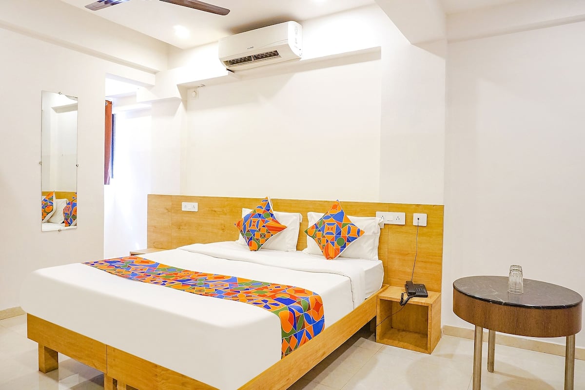 A modern hotel room with a wooden bed, a round side table, and a small bedside table with a lamp.