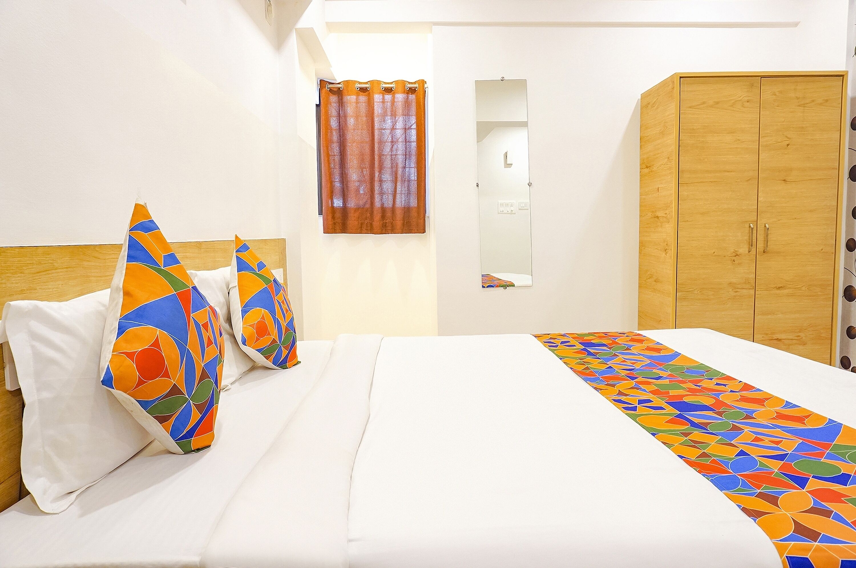 Ein Hotelzimmer mit Bett, bunten Kissen, einem Holzschrank und einem Badezimmerspiegel.
