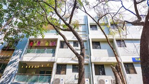 A multi-story building with balconies, air conditioning units, and a tree in front.