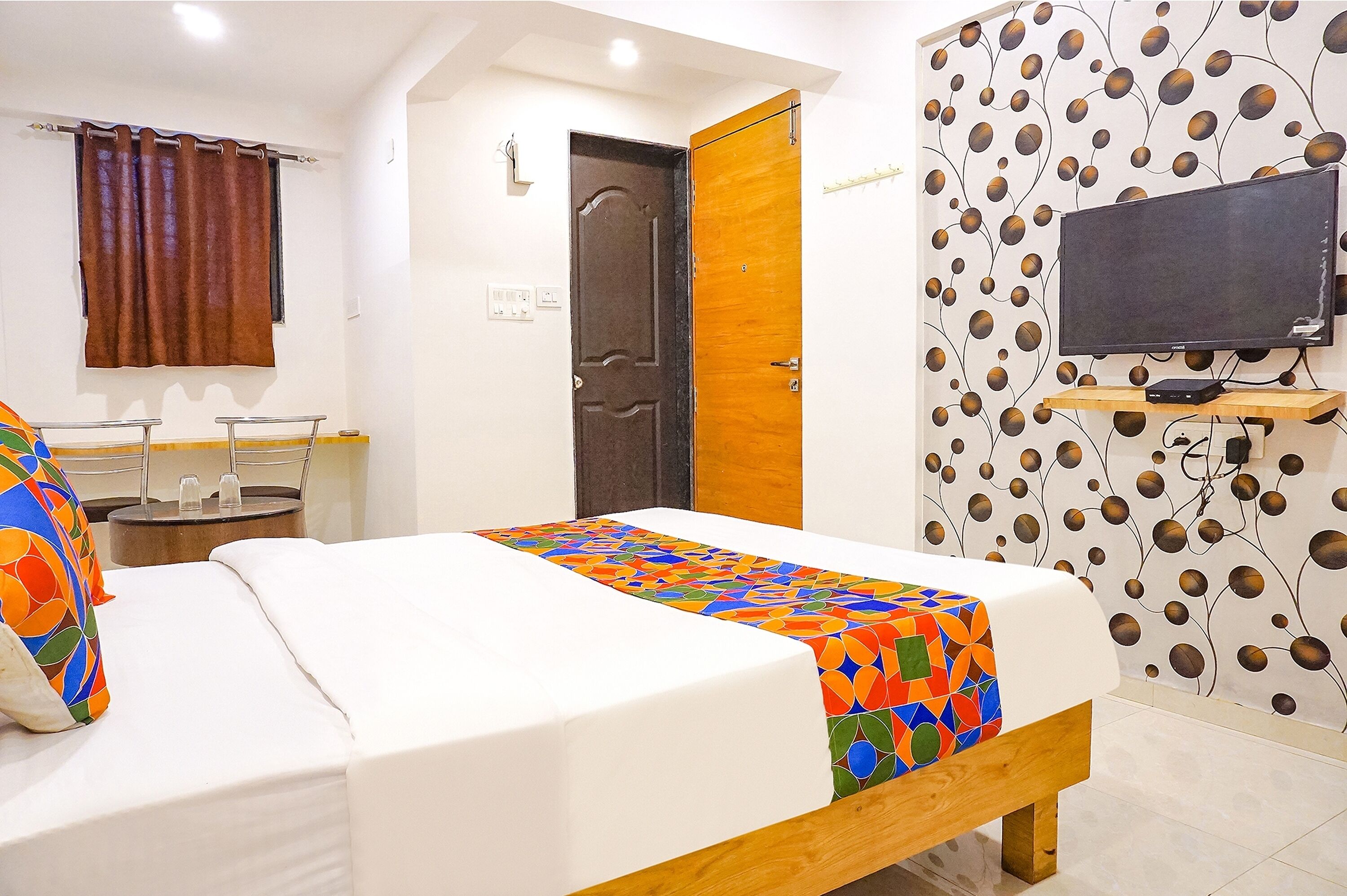 Une chambre d’hôtel avec un lit, un téléviseur fixé au mur, une porte en bois et un papier peint à motifs.