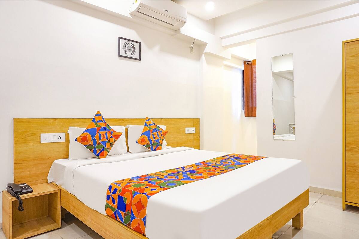 A neatly made bed with a colorful blanket, a bedside phone, and a wooden nightstand.