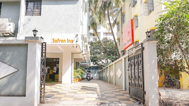 A hotel entrance with a checkered pavement leading to the door, a sign for 'Safron Inn', and a gated area with a motorcycle parked outside.