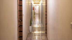 A long, well-lit hallway with a polished marble floor, wooden panel ceiling, and a potted plant. - Hotel Royce Executive (Mumbai)