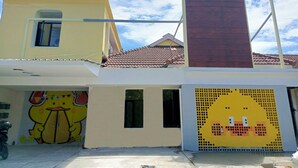 A two-story building with a yellow facade, a brown roof, and a cartoon mural on the lower wall. - Bebek Kuning Residence (Malang)