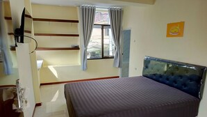 A bedroom with a bed, a window with curtains, a television, and a wall-mounted picture. - Bebek Kuning Residence (Malang)