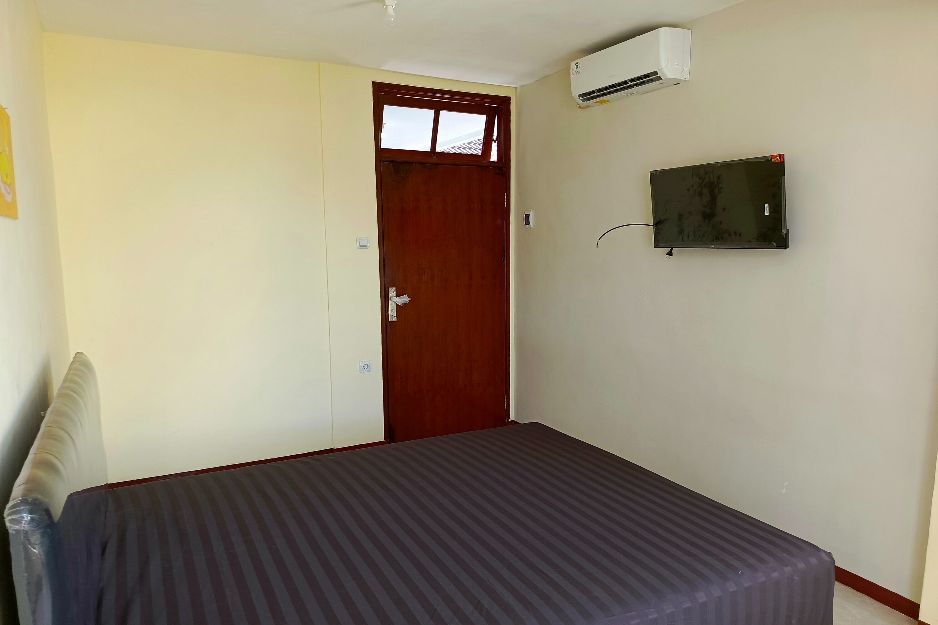 A room with a bed, a wooden door, an air conditioning unit, and a mounted television.