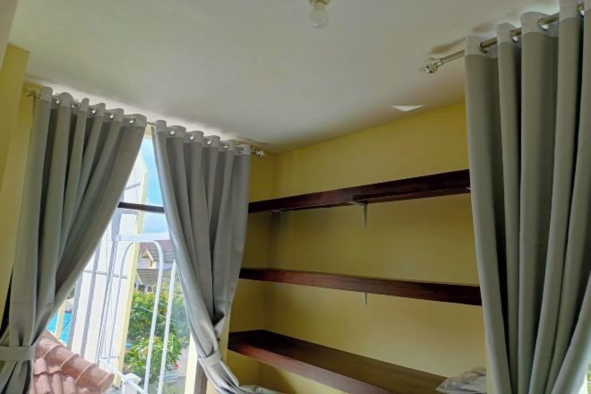 Una stanza con una parete gialla, una ventola a soffitto e una finestra con tende.