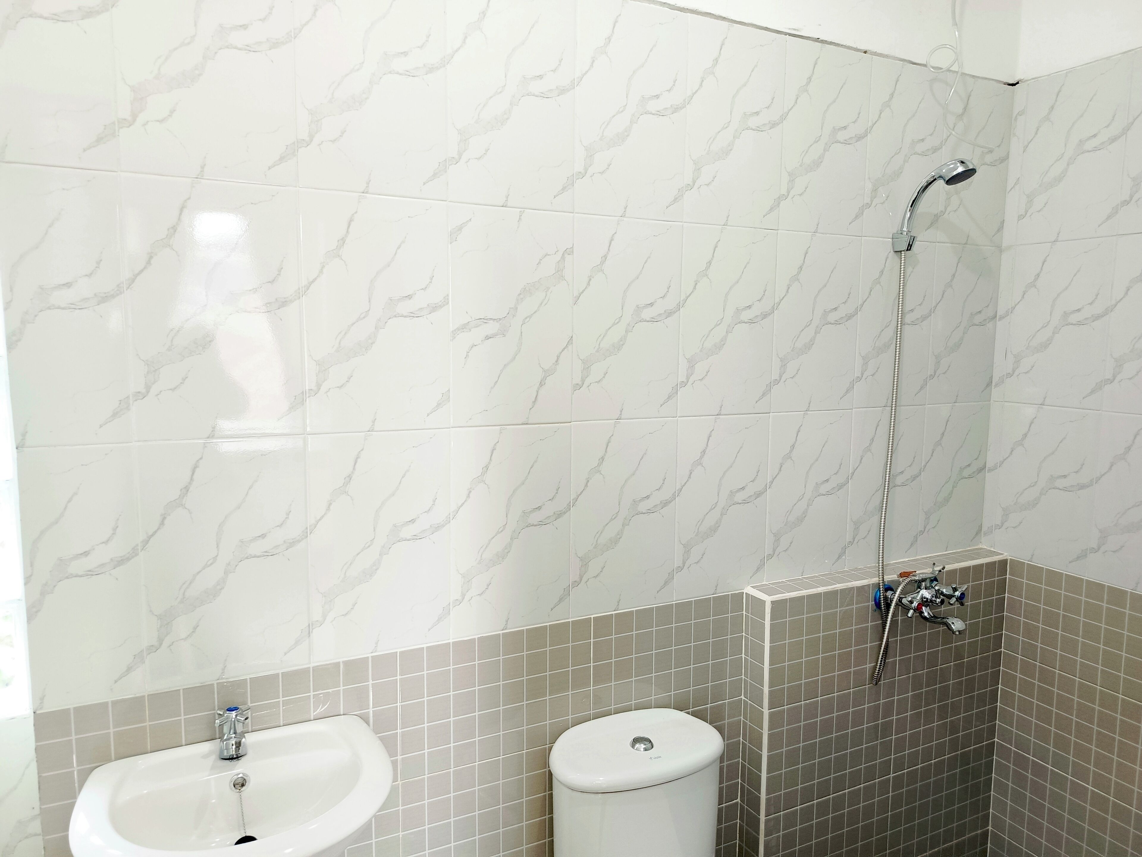 A bathroom with marble-patterned walls, a sink, a toilet, and a shower.