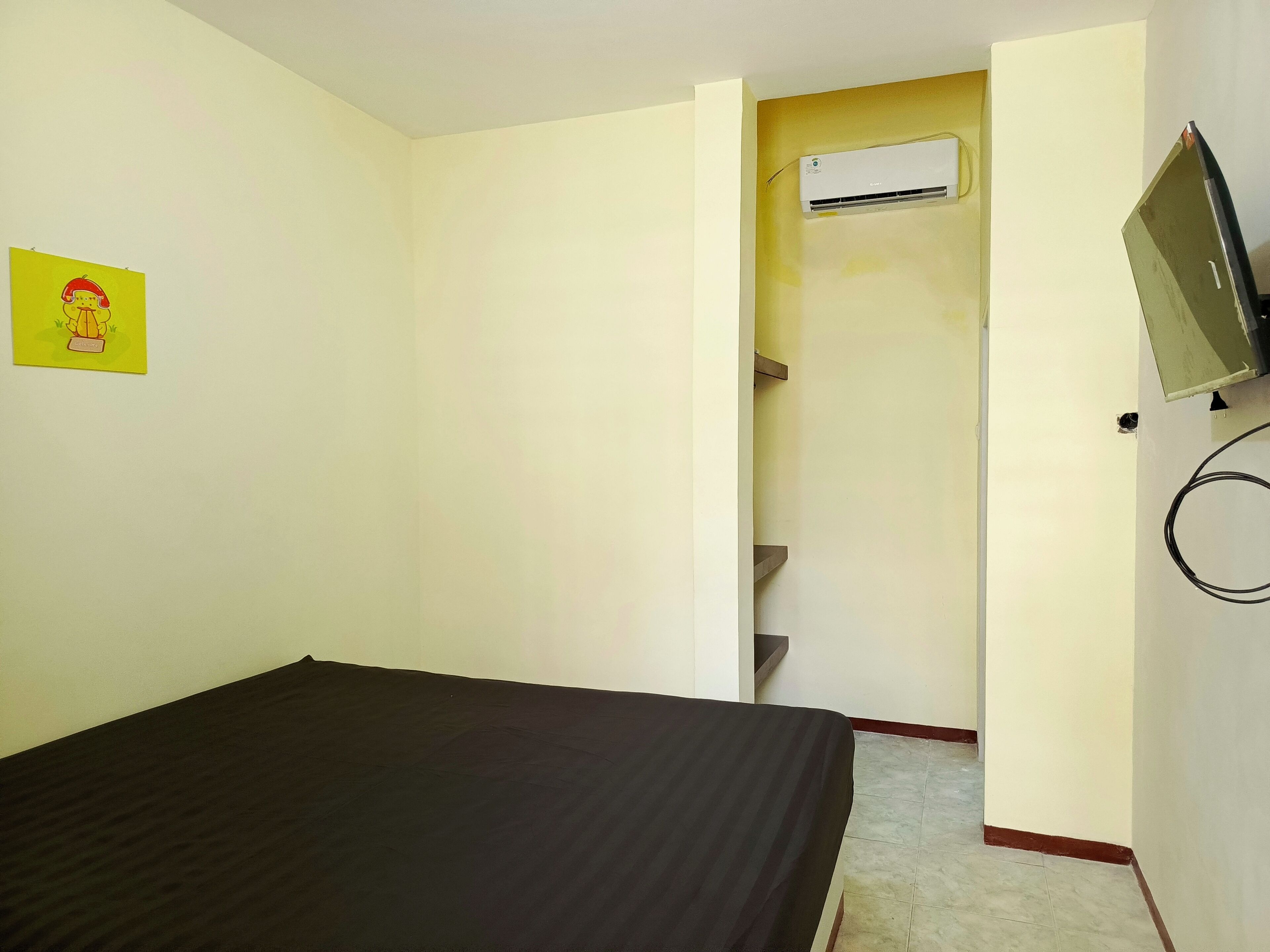 A room with a bed, an air conditioning unit, a television, and a small shelf.