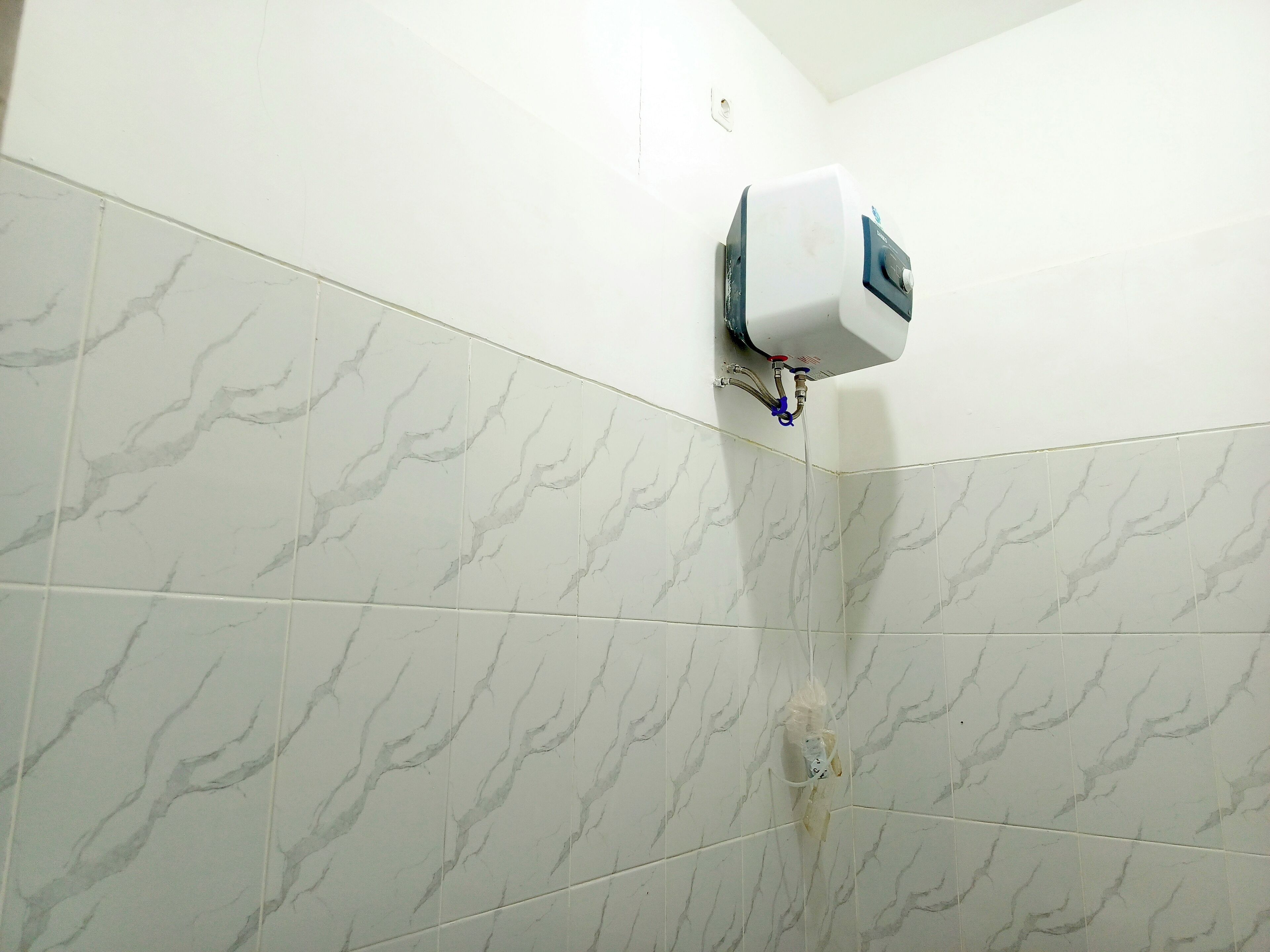 A bathroom with white marble tiles and a wall-mounted water dispenser.