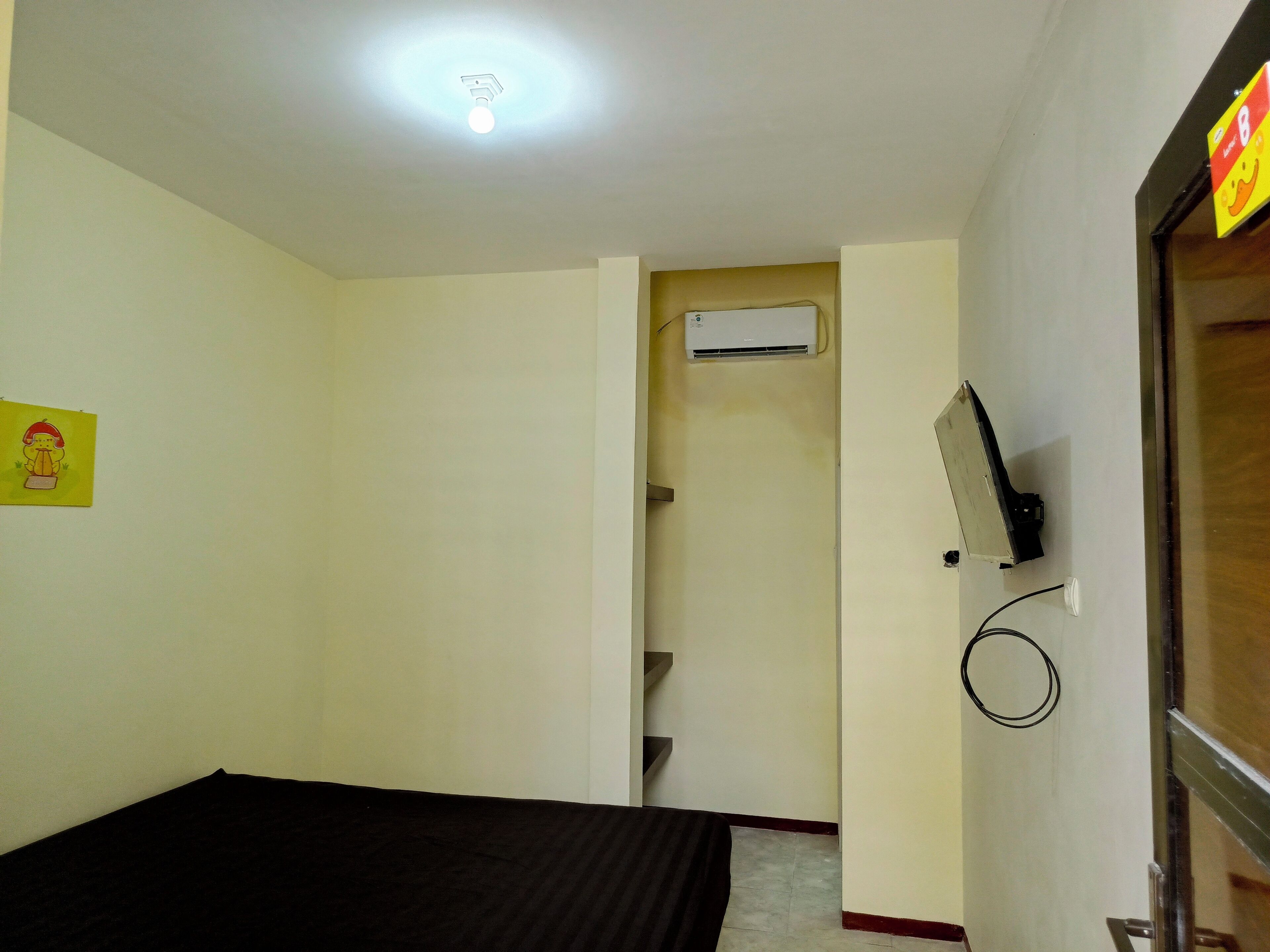 A room with a bed, an air conditioning unit, a wall-mounted TV, and a door leading to a staircase.