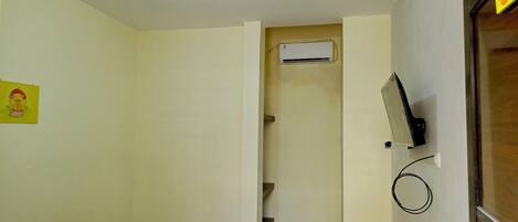 A room with a bed, an air conditioning unit, a wall-mounted TV, and a door leading to a staircase.