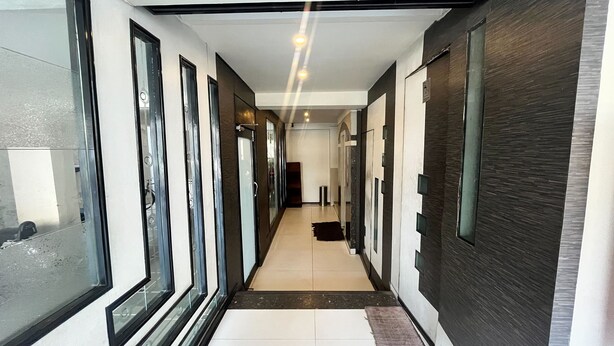 A modern hallway with glass doors, a tiled floor, and a dark wooden accent wall.