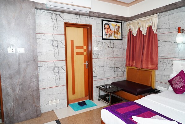 A bedroom with a bed, a bedside table, a nightstand, a wooden door, and a window with curtains.
