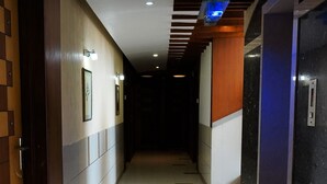 A hotel corridor with a tiled floor, wooden and metal walls, and a glass elevator.