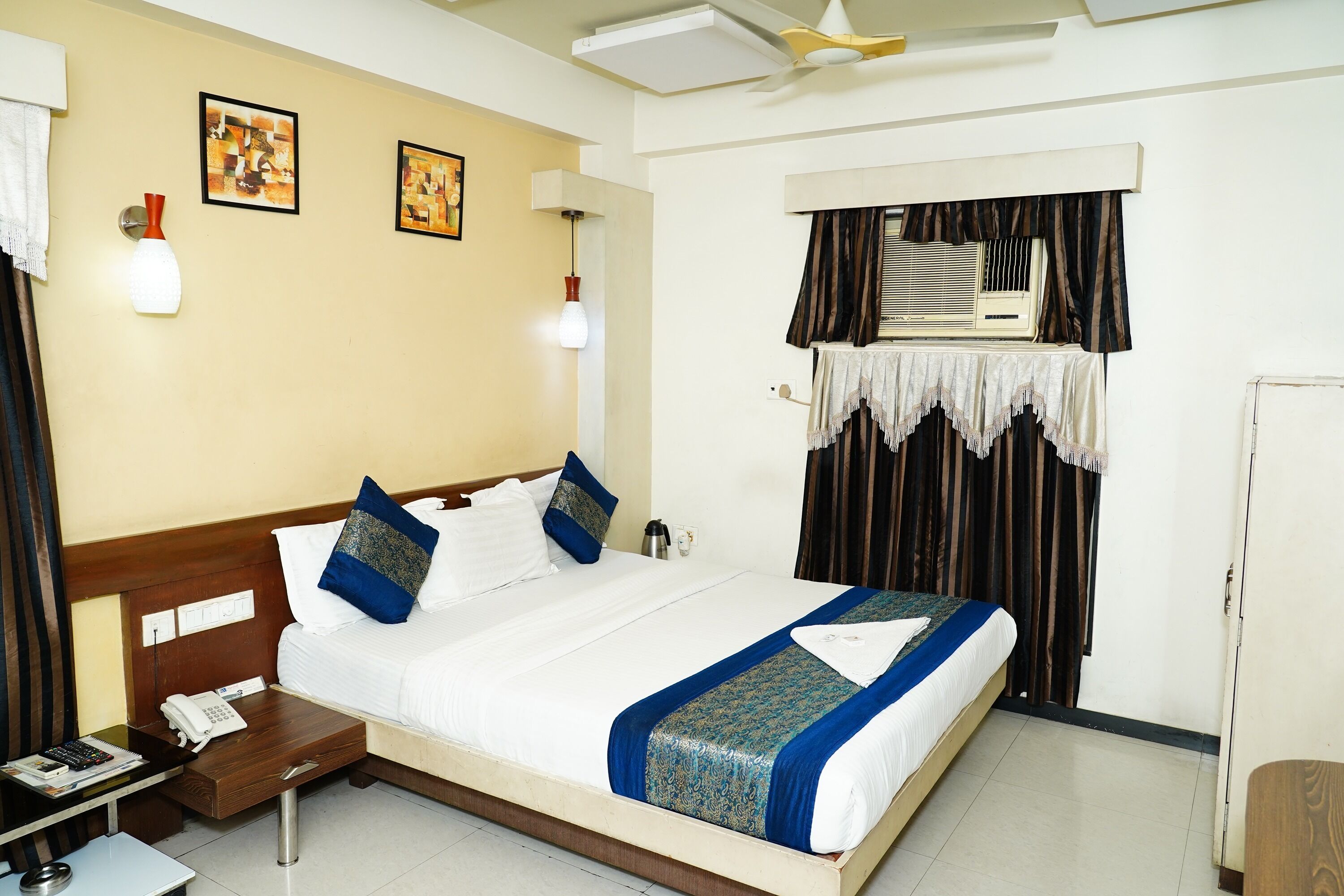 A hotel room with a large bed, bedside tables, a desk, a telephone, and a window with curtains.