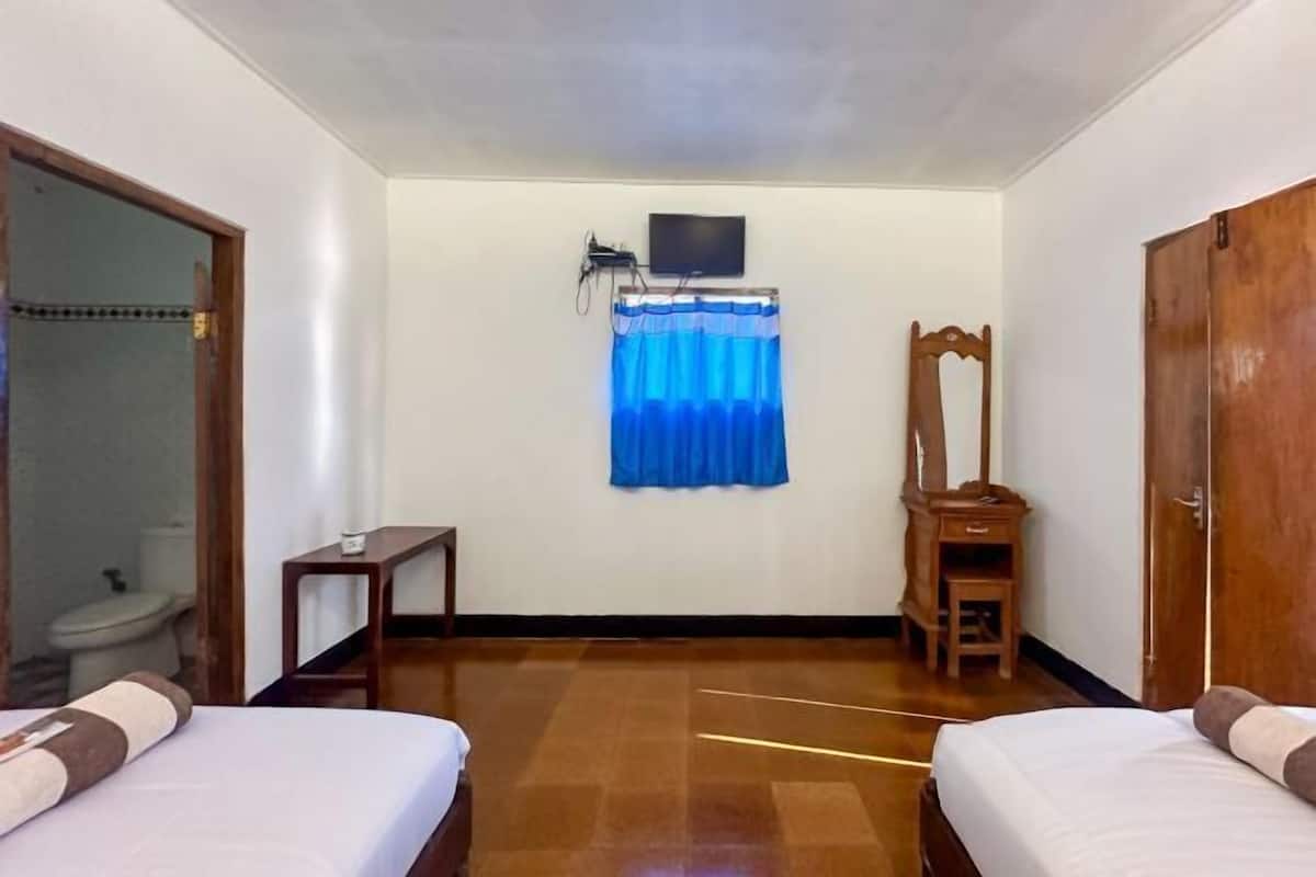 Ein Hotelzimmer mit zwei Betten, einem kleinen Tisch, einem Stuhl, einem Spiegel und einem Fernseher an der Wand.