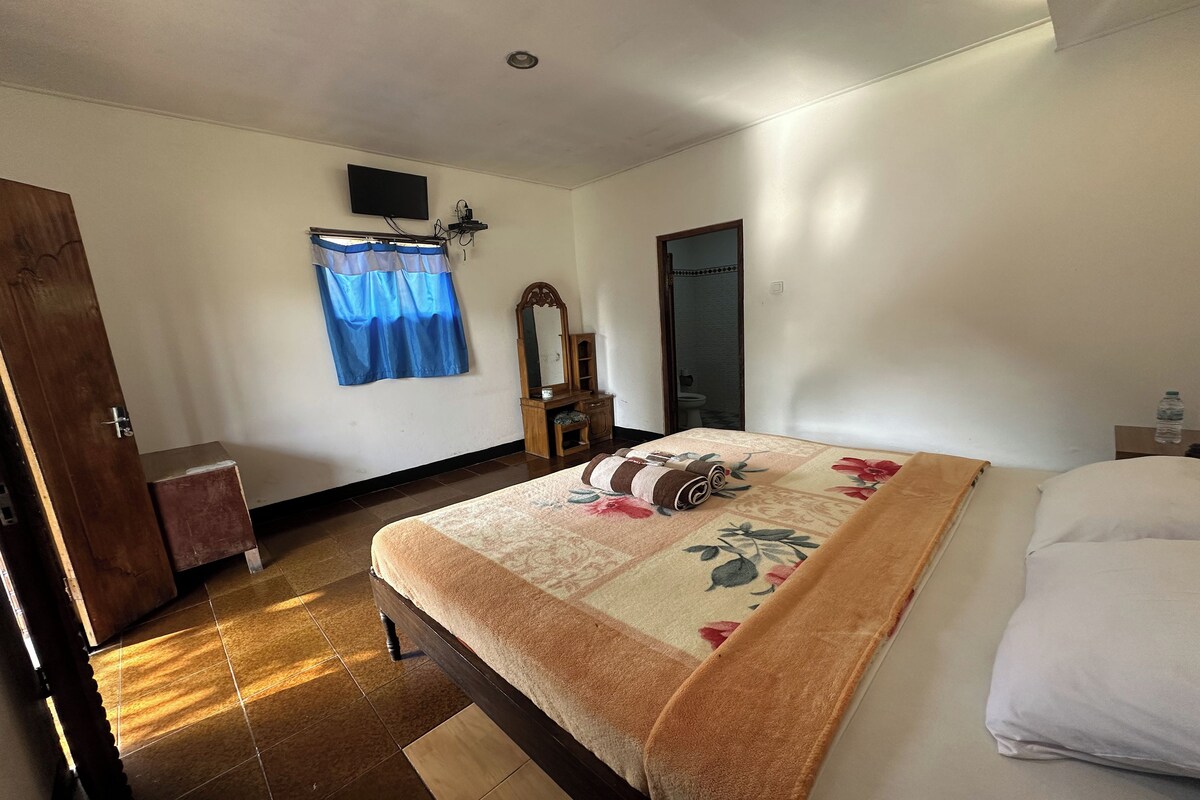 Une chambre à coucher comprenant un lit, une armoire en bois, une petite table, un miroir et un téléviseur fixé au mur.
